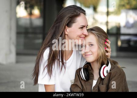 Mutter umarmt sich mit der Tochter im Freien. Fröhlicher Teenager und Frau in guter Laune. Liebe und Familienkonzept Stockfoto