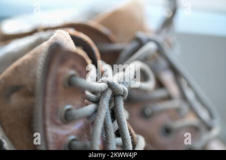 Nahaufnahme alter Arbeitsstiefel aus verwittertem braunem Leder mit Schnürsenkeln, die mit Schleife und Schuhdetail verbunden sind Stockfoto