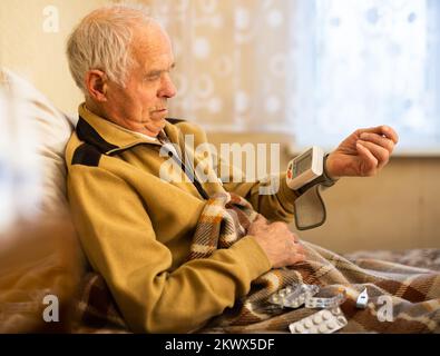 Alter Mann in eine Decke gewickelt, die den Druck mit Tonometer misst Stockfoto