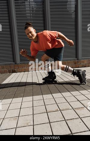 Positiver Mann, der auf die Kamera schaut, während er Rollschuhlaufen auf der Straße, Stockbild Stockfoto