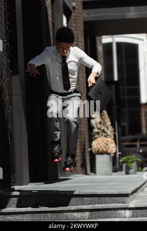 Geschäftsmann in Rollschuhen und Helm mit Aktentasche, während er auf der Straße von der Treppe springt, Stockbild Stockfoto
