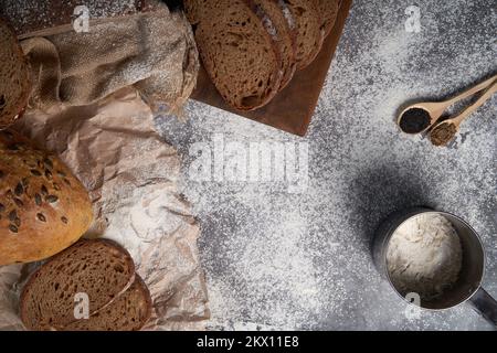 Draufsicht auf verschiedene Brotsorten, geschnitten und ganz, Mehl, zerknittertes Papier und Latte auf einem Holztisch. Flach verlegt. Stockfoto