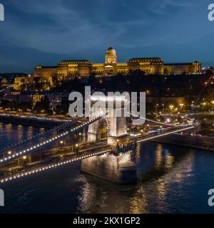 Blick auf den Buda-Palast und die Szechenyi-Kettenbrücke über die Donau bei Abenddämmerung in Budapest, Ungarn. Stockfoto