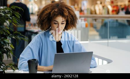 Frontsicht fokussiert Millenials afroamerikanische Geschäftsfrau Freiberufler Manager Spezialist sitzt am Tisch im Café und arbeitet mit Laptop Stockfoto