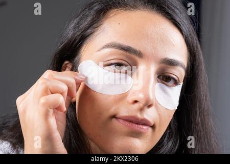 Unter Augenklappe verwenden, Nahaufnahme, kein Make-up, natürliches Gesicht. Kaukasische braune Millenial-Frau, kämpft mit dunklen Kreisen. Schwellungen, Falten, Wohlbefinden. Stockfoto