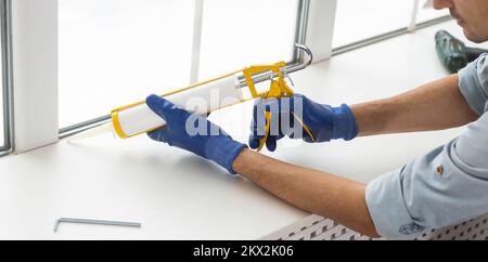 Bauarbeiter versiegelt Fenster mit Versiegelung in Innenräumen Stockfoto