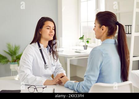 Junge weiße Frau Ärztin im weißen Kittel tröstet Patienten Krankenhausaufenthalt und hält Hand Stockfoto