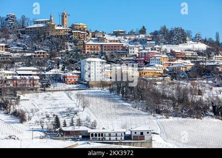 Blick auf die kleine Stadt auf einem schneebedeckten Hügel unter blauem Himmel in Piemont, Norditalien. Stockfoto