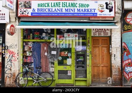 Mit Graffiti überdachter Laden vor einem islamischen Laden und Minimarkt in Brick Lane, Shoreditch, London Stockfoto