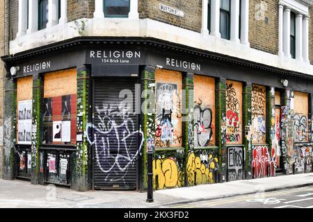 Religionsladen mit verkleideten Fenstern und Fensterläden bedeckt mit Graffiti an der Ecke Buxton Street und Brick Lane in Shoreditch, London Stockfoto