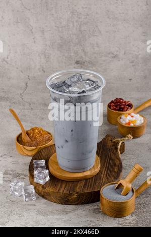 Boba- oder Tapioka-Perlen sind taiwanesischer Seifenmilchtee in Plastikbecher mit Kohlegeschmack auf Texturhintergrund, Sommererfrischung. Stockfoto