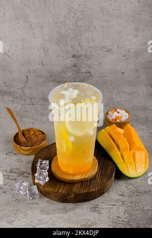Boba- oder Tapiokapperlen ist taiwan Seifenmilchtee in Plastikbecher mit Mango-Zitronen-Aroma auf texturiertem Hintergrund, Sommererfrischung. Stockfoto