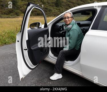 Eine grauhaarige Frau steigt aus dem Auto und lächelt in die Kamera Stockfoto