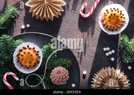 Dunkler Winterhintergrund mit duftenden Pomanderbällen. Klassische Dekoration - Mandarine mit Nelken. Handgefertigte Papiersterne aus braunem Backpapier Stockfoto