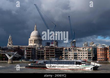 Ein Uber-Boot von Thames Clippers, ein Flussbus, der unter der Millennium-Brücke vorbeifährt, bevor er am Bankside Pier, St. Die Pauls Cathedral ist im zu sehen Stockfoto