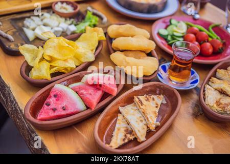 Türkischer Frühstückstisch. Gebäck, Gemüse, Gemüse, Gemüse, Oliven, Käse, Spiegeleier, Gewürze, Marmelade, Honig, Tee in Kupfertopf und Tulpengläser, breit Stockfoto