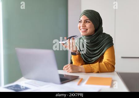 Junge Muslimische Frau In Hijab Nimmt Sprachnachricht Auf Smartphone Im Büro Auf Stockfoto