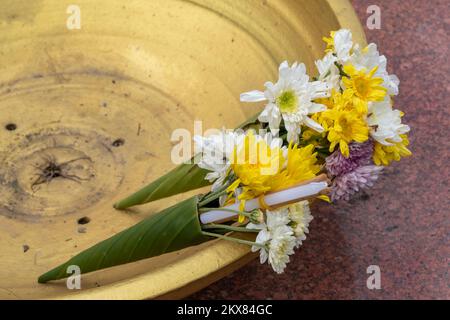 Traditionelles Angebot an Chrysanthemen, Kerzen und Räucherstäbchen in Bananenblättern in einer goldenen Schüssel im buddhistischen Tempel in Thailand Stockfoto