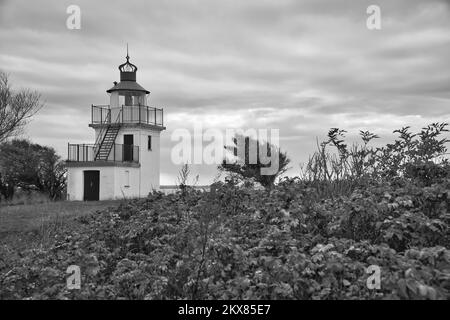 Schwarzweißer Leuchtturm, Spodsbjerg Fyr in Huntsted an der Küste Dänemarks. Die Sonne scheint durch die Wolken. Wiese mit Bäumen. La Stockfoto