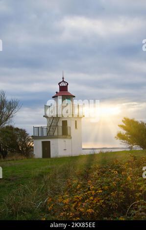 Leuchtturm, Spodsbjerg Fyr in Huntsted an der Küste Dänemarks. Die Sonne scheint durch die Wolken. Wiese mit Bäumen. Landschaftsfoto vom Meer Stockfoto