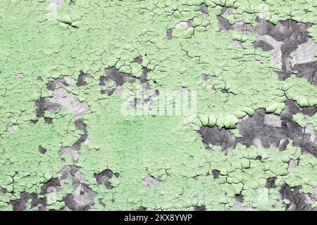 Grüne Farbe blättert von der Wand ab. Blick auf eine Betonwand mit alter rissiger abblätternder Farbe. Stockfoto