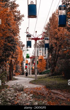 Farbenfrohe Kabinen im Herbstpark mit goldenen Bäumen und grauem Himmel. Farblich abgestuft Stockfoto