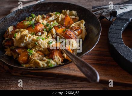 Geröstete Süßkartoffeln mit Rührei, Schnittlauch und Petersilie in einem rustikalen Topf. Gesunde Muskelaufbau Fitness-Mahlzeit Stockfoto