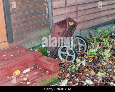 Hauseingang, braune Blätter auf dem Boden und verlassener Gartenwagen, Fokus im Vordergrund Stockfoto