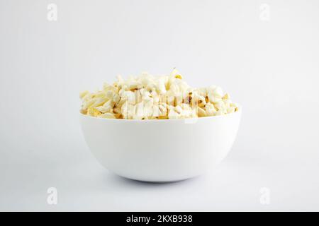 Popcorn in einer weißen Schüssel, isoliert auf weißem Hintergrund. Selektiver Fokus. Maissnacks. Stockfoto