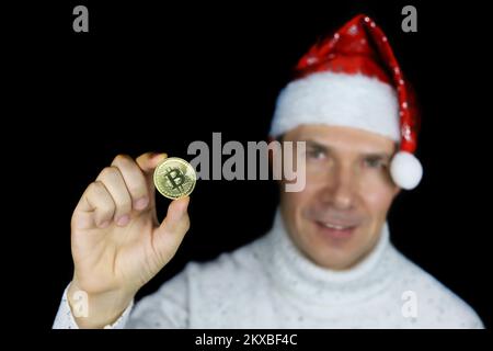 Porträt eines glücklichen Mannes mit Weihnachtsmannmütze mit Bitcoin in der Hand auf schwarzem Hintergrund. Weihnachtsfeier, elektronisches dezentralisiertes Geld, Krypto-Währung Stockfoto