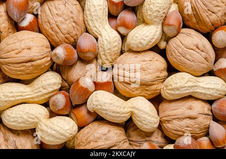 Gemischte Nüsse in ihren Schalen, Snacknüsse, Hintergrund. Haselnüsse ohne Schale, Erdnüsse und Walnüsse, getrocknet und verzehrfertig. Stockfoto