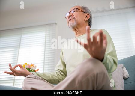 Ein alter asiatischer Mann übt Yoga und Meditation in Lotusposition und mit geschlossenen Augen Stockfoto