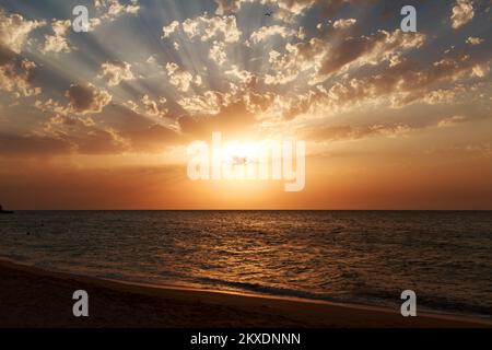 Wellen auf dem Meer bei Sonnenuntergang. Entspannung, Vergnügen. Reise zum Meer, Frieden und Glück. Farbenfroher, heller, orangefarbener Sonnenuntergang. Die Sonne scheint durch die Wolken auf dem Ozean. Schöne Tapeten für dein Handy. Hochwertige 4K-Aufnahmen. Stockfoto