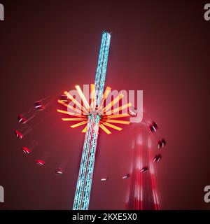 Die 60 Meter hohe Star Flyer-Fahrt bei Nacht während der Blackpool Christmas Funfair mit dem von Nebel ummantelten Blackpool Tower Stockfoto