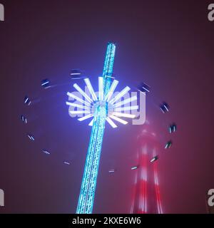 Die 60 Meter hohe Star Flyer-Fahrt bei Nacht während der Blackpool Christmas Funfair mit dem von Nebel ummantelten Blackpool Tower Stockfoto