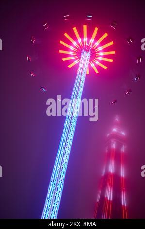 Die 60 Meter hohe Star Flyer-Fahrt bei Nacht während der Blackpool Christmas Funfair mit dem von Nebel ummantelten Blackpool Tower Stockfoto