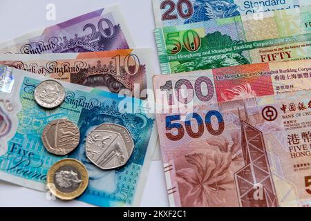 Nahaufnahme von Hong Kong Dollar-Banknoten und britischen Sterling-Banknoten und -Münzen, isoliert auf weißem Hintergrund. Stockfoto