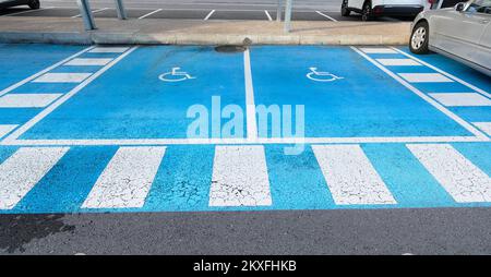 Für Behinderte reservierter doppelter kostenloser Parkplatz auf blauem Asphalt mit dem internationalen Behindertensymbol in Weiß mit dem hellen Blau von Stockfoto