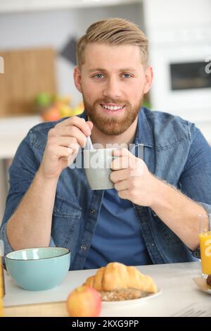 Lächelnder bärtiger Mann mit einer Tasse Morgenkaffee und Croissant Stockfoto