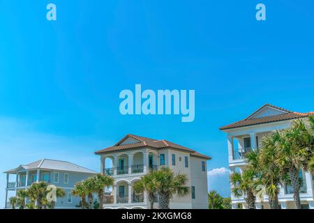 Destin, Florida - Vorderseite von Strandhäusern vor dem blauen Himmel. Drei Strandhäuser mit Palmen vor den Balkonen. Stockfoto