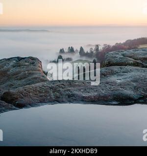 Ungewöhnliche Aussicht von der Spitze der Cow and Calf Rocks in Ilkley während einer Wolkeninvertierung mit Nebel, der durch Bäume schwebt und eine Pfütze im Vordergrund Stockfoto