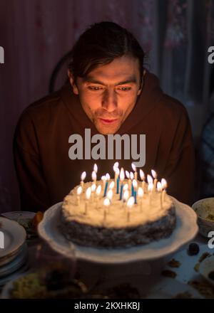 Ein junger Mann bläst die Kerzen auf dem Kuchen aus, um die Geburtstagsparty zu feiern Stockfoto