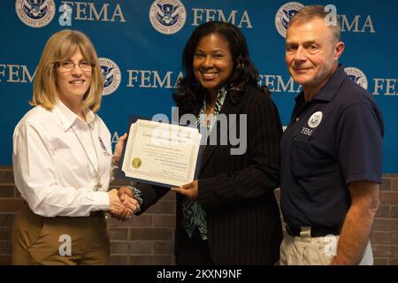 Flooding Hurricane/Tropical Storm - Neptune, N. J. , 16. November 2011 Sandra May (Center), Senior Media Representative für Atlantic City Electric, stellt ein Dankeszertifikat vor, das an die FEMA für ihren Beitrag zum Erfolg der Disability Awareness Expo von Pepco Holdings Inc. Ausgestellt wurde. Die Präsentation fand am Ende einer Tour des Gemeinsamen Feldbüros (JFO) der FEMA in Neptun statt. Die Tour wurde von Bill Vogel (rechts), Federal Coordinating Officer, und Susan Langhoff (links), Assistant External Affairs Officer for Private Sector, geleitet. Die FEMA fördert die Beteiligung der privaten Sekte Stockfoto