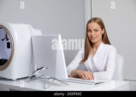 Lächelnde junge Ärztin, die bei der Konsultation mit ihrem Computer arbeitet Stockfoto