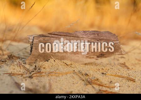 Konzept, Wirtschaft und Finanzen. Im Sand vor dem Hintergrund von gelbem Gras gibt es ein Schild mit der Inschrift - CODE OF ETHICS Stockfoto