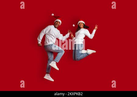 Ein emotionales schwarzes Paar, das auf Rot springt und Weihnachten feiert Stockfoto