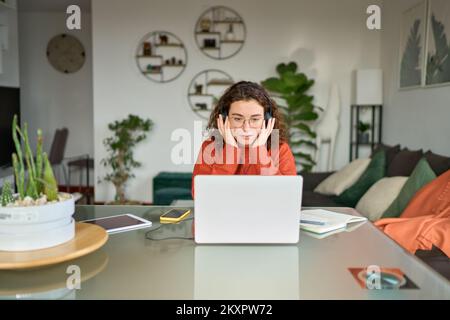 Junge Frau mit Kopfhörern, die ein Notebook benutzt und sich ein Online-Webinar ansieht, das zu Hause lernt. Stockfoto