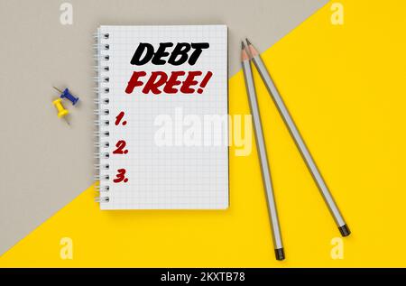 Wirtschaft und Finanzen. Auf einem gelb-grauen Hintergrund sind Bleistifte, Knöpfe und ein Notizbuch, in dem es geschrieben ist - SCHULDENFREI Stockfoto