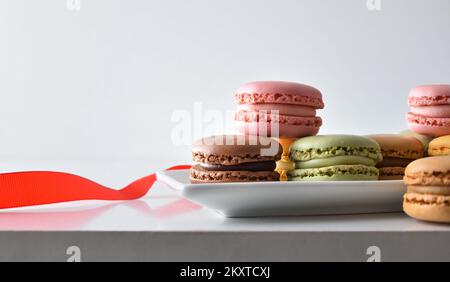 Auswahl französischer Makronen verschiedener Geschmacksrichtungen auf weißem Teller mit rotem Band und heller isolierter Hintergrundfarbe. Vorderansicht. Stockfoto