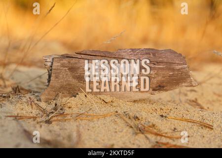 Bildungs- und Wissenschaftskonzept. Auf dem Sand vor einem Hintergrund mit gelbem Gras, ein Schild mit der Inschrift - LEKTIONEN GELERNT Stockfoto